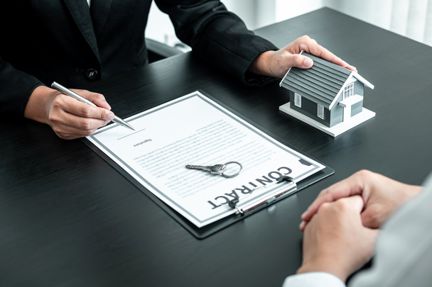 Makelaar werken ondertekenen contract document contract voor woningkredietverzekering goedkeuring van aankopen voor klant met huismodel en sleutel op tafel. - Foto, afbeelding
