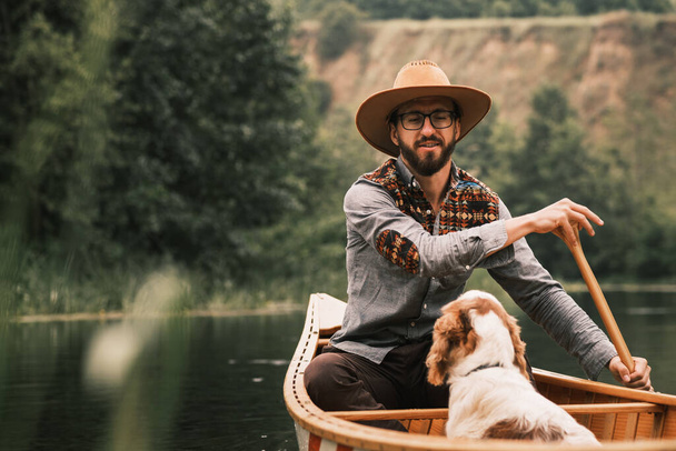 Хмурый человек и собака, бродящие на каноэ по реке - Фото, изображение