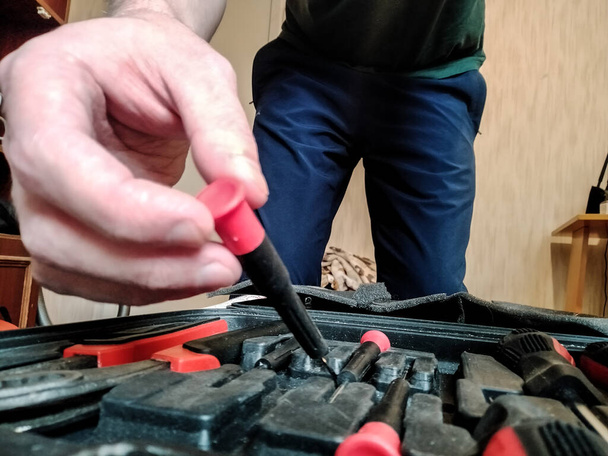 electricista macho saca un pequeño destornillador en el trabajo de una maleta con herramientas - Foto, Imagen