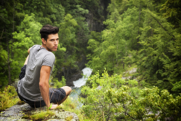 Handsome young man sitting in lush green mountain scenery - Фото, изображение
