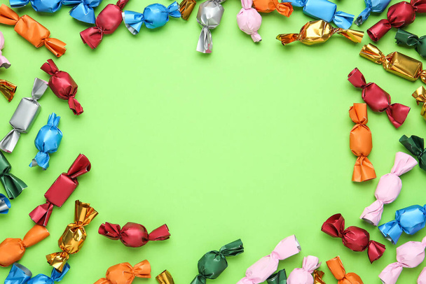 Frame of candies in colorful wrappers on light green background, flat lay. Space for text - Zdjęcie, obraz