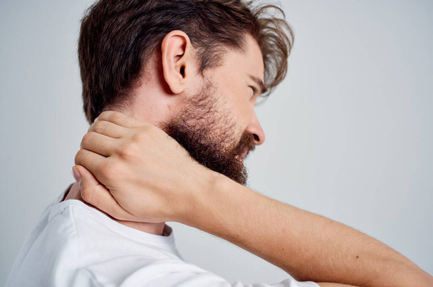bärtiger Mann im weißen T-Shirt Stress Medizin Schmerzen im Nacken Licht Hintergrund - Foto, Bild