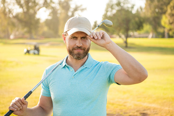 Άντρας παίκτης του γκολφ σε επαγγελματικό γήπεδο γκολφ. πορτρέτο του παίκτη του γκολφ στο καπέλο με μπαστούνι του γκολφ. - Φωτογραφία, εικόνα