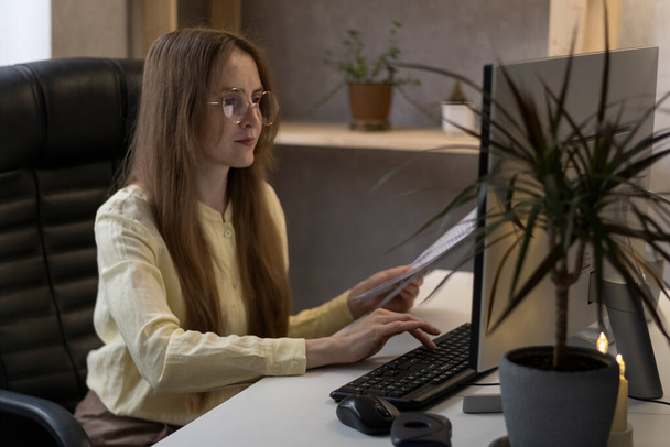 A fiatal könyvelőnő a számítógépnél dolgozik és dokumentumokat tart magánál. A főnök saját irodájában van. A titkár adatokat visz be a programba. - Fotó, kép
