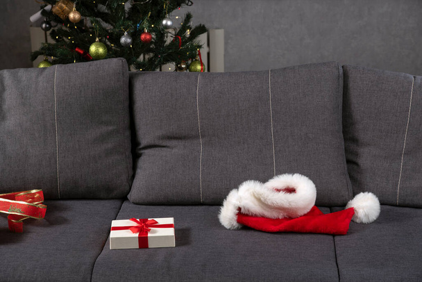 Sombrero de Santa y caja de regalo abierta en sofá gris. Fin de Año Nuevo. - Foto, imagen