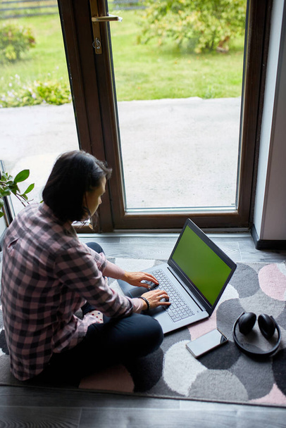 Freelancer vrouw typen op laptop zitten op de vloer thuis in de buurt van grote ramen, Content vrouw browsen notebook, studeren, werken vanuit huis. - Foto, afbeelding