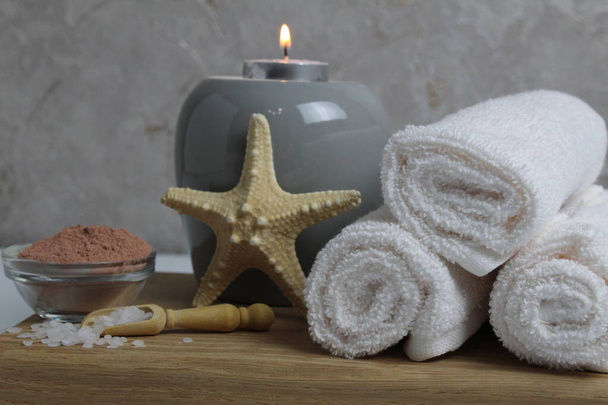 Spa détente massage maison soin du corps. Serviettes blanches huile parfumée pour massage aromathérapie bougies étoile mer se trouvent sur un plateau en bois sur un fond gris vue latérale. - Photo, image