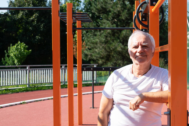 Veilige outdoor oefeningen voor ouderen Volwassenen senior man zomer, straat workout fysieke Kracht activiteit in Calisthenics Park - Foto, afbeelding