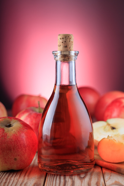 Бутылка яблочного сидра и красные яблоки на деревянном фоне, освещенном красным светом. Мягкий фокус. - Фото, изображение