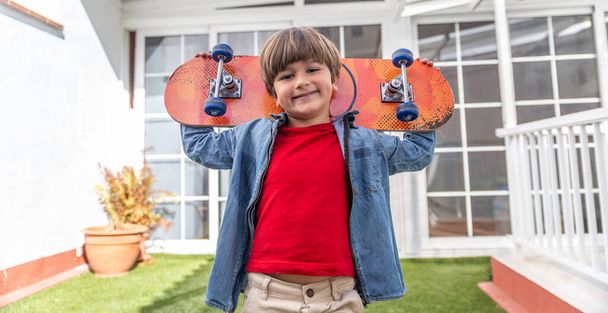 Happy and relaxed boy with his skateboard on his back in the garden of his house - Φωτογραφία, εικόνα