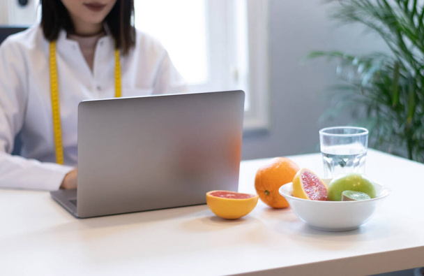 donna dietista che lavora con il suo computer e un ufficio con frutta mista e acqua sul tavolo - Foto, immagini