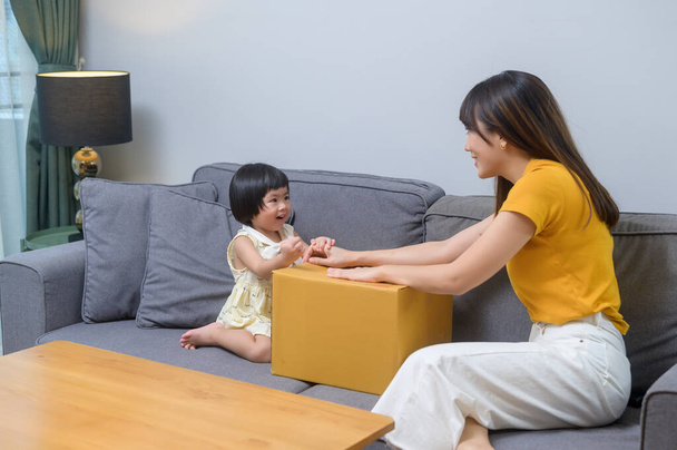 A happy mom with daughter opening cardboard box in living room at home - Foto, afbeelding