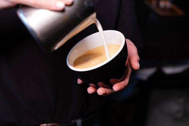 latte art van barista. melk in koffie gieten. donker koffiehuis - Foto, afbeelding