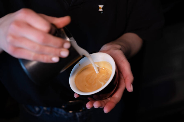 Barista giet latte foam op koffie, espresso. het creëren van een perfecte latte kunst. donkere kleuren, koffiehuis - Foto, afbeelding