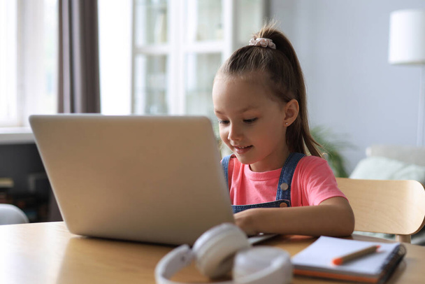 Distance learning. Cheerful little girl girl in headphones using laptop studying through online e-learning system - Foto, Imagen