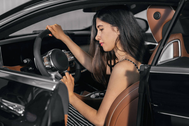 Young asian woman sitting in luxury car in garage before starting engine - Photo, Image