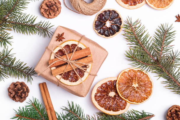 Christmas composition with handmade kraft paper gift box, dried citrus slices, cinnamon, anise, pine cones and fir tree branches, top view close up - Photo, Image