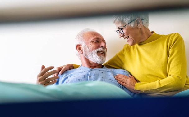 Mature couple in love. Happy senior woman visiting her husband in hospital ward. Healthcare people support concept - Фото, изображение