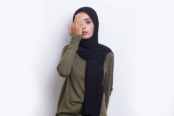 Jeune femme musulmane asiatique couvrant un oeil avec la main isolé sur fond blanc - Photo, image