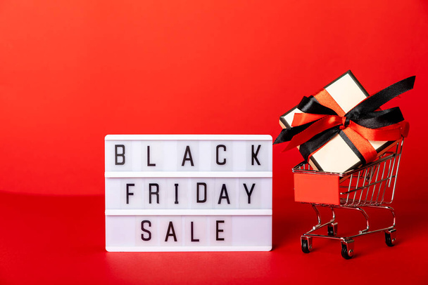 red basket with a gift box on a red background, lettering Black Friday, with copy space. - Φωτογραφία, εικόνα