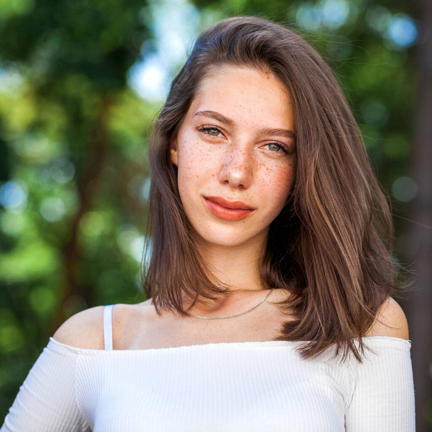 Portrait of a young beautiful brown-haired girl with freckles on her face - Foto, Imagen