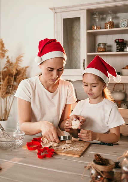 cheerful mom and daughter in Christmas hats play at the table in the kitchen - Photo, Image