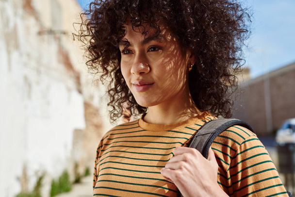 Beautiful young black woman walking alone with a backpack outdoors during the day - Фото, изображение