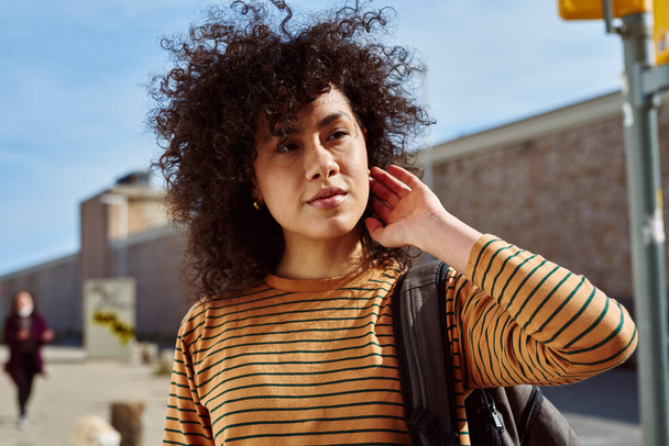 Cute young black woman touching her hair while standing with a backpack outdoors during the day - Zdjęcie, obraz