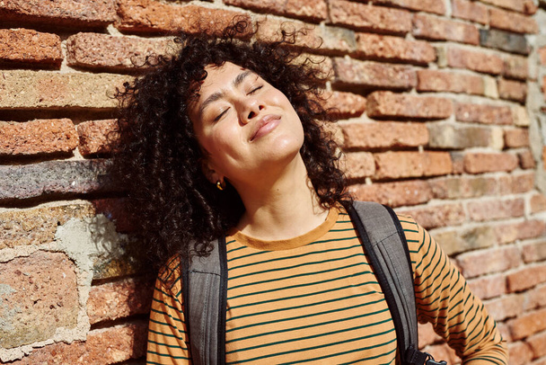 Cute young black woman leaning against a brick wall with her eyes closed outdoors during the day - Fotografie, Obrázek