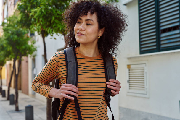 Cute young black woman looking away while walking with a backpack outdoors during the day - Foto, Bild