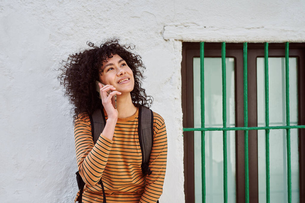 Smiling young black woman speaking on the phone while standing against a brick wall outdoors during the day - Фото, зображення