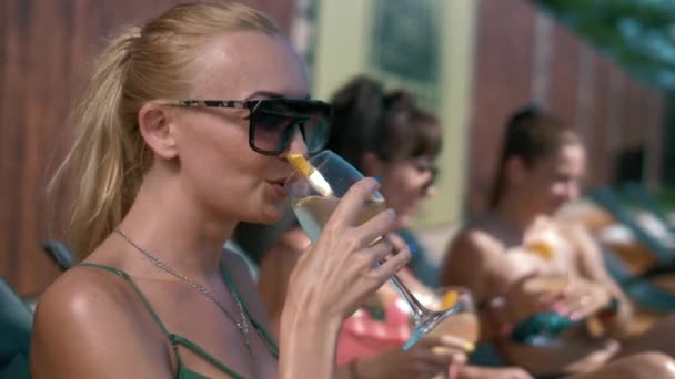 Hermosas chicas bronceadas beben cócteles en tumbonas junto a la piscina - Metraje, vídeo