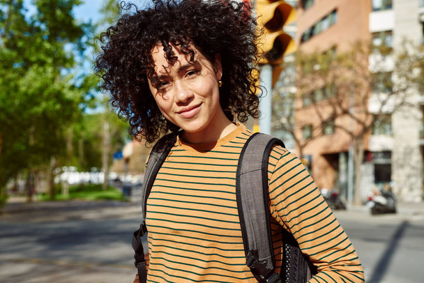 Attraktive junge schwarze Frau mit Rucksack, die tagsüber im Freien in die Kamera schaut - Foto, Bild