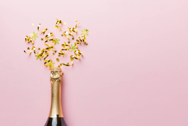 Creative flat lay composition with bottle of champagne and space for text on color background. Champagne bottle with colorful party streamers. holiday or christmas concept. - Photo, Image