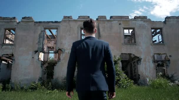 自然災害によって破壊された住宅の建物の背景に古典的なスーツの男性 - 映像、動画