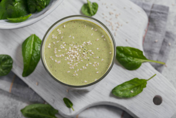 Szklanka domowego zdrowego zielonego smoothie ze świeżym szpinakiem dla dzieci i nasionami sezamu na jasnym tle. Jedzenie i picie, dieta i koncepcja zdrowego odżywiania - Zdjęcie, obraz
