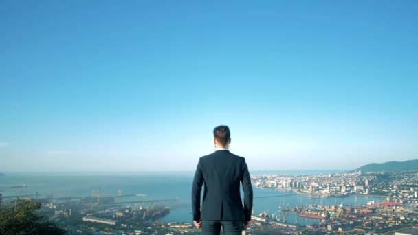 Un exitoso hombre de negocios con chaqueta se para y mira a la ciudad desde la vista de un pájaro - Metraje, vídeo