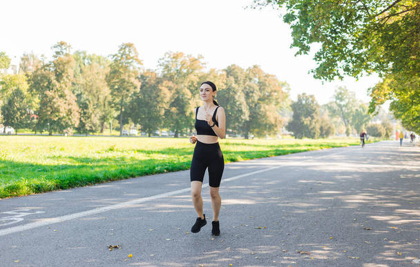 Athlétique jeune femme heureuse qui court dans le parc jogging le matin pour la santé de style de vie. Entraînement extérieur. Sport et mode de vie sain et actif. - Photo, image