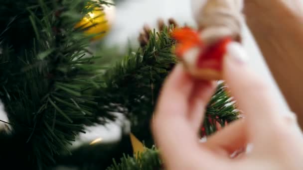 Jong meisje hangt een leuke houten pop aan de kerstboom. Close-up, hand - Video