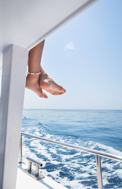 Close-up of beautiful female legs with a bracelet with shells on a yacht, sailing on a yacht, summer vacation, conceptual image of pleasure and enjoyment. Vacation, sea and ocean rest - Photo, Image