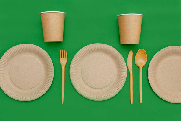 Recyclable fork, spoon, knife, plate and cup on a green background. Kitchen utensils are served on the table. Top view. Minimalist Style. Copy space. - Foto, afbeelding