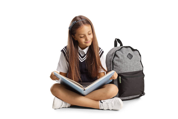 Schoolgirl sitting on the floor and reading a book isolated on white background - Photo, Image