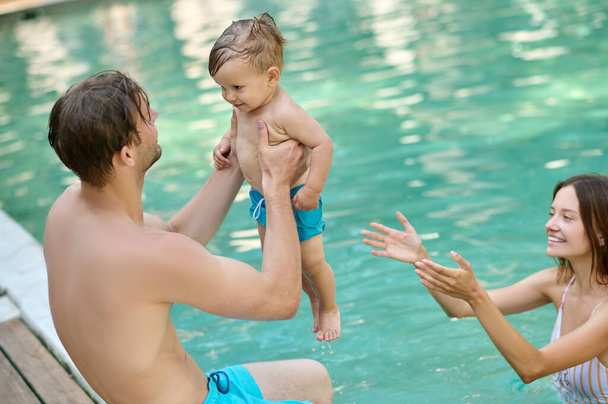 A young family spending time in a summer swimming pool - Foto, afbeelding
