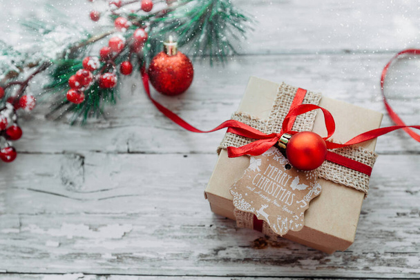κουτί δώρου και χριστουγεννιάτικα στολίδια σε ξύλινο φόντο με νιφάδες χιονιού. - Φωτογραφία, εικόνα
