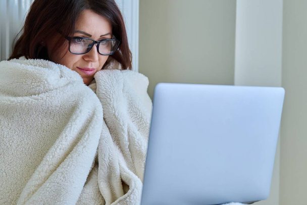 Woman working at home with laptop, warming with blanket and heating radiator - Photo, Image