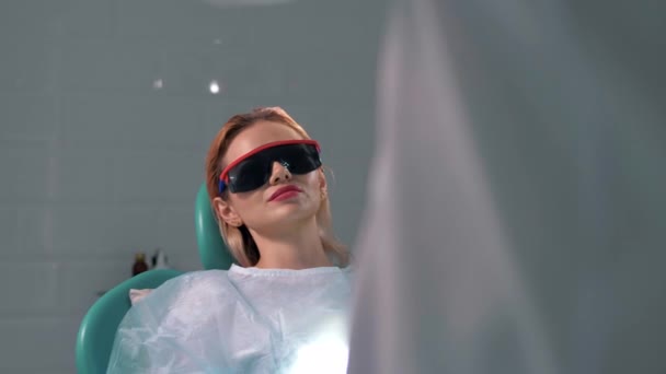 Piękna dziewczyna w ciemnych okularach na przyjęciu w klinice stomatologicznej - Materiał filmowy, wideo