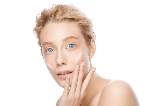 Young beautiful blonde woman with clear skin applying face cream with fingers, isolated on white - Fotoğraf, Görsel