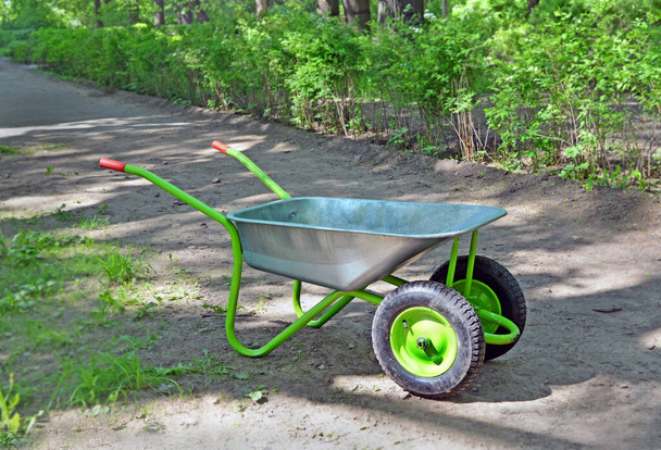 Bahçedeki yolda iki yeşil tekerleği olan boş bahçe el arabası ya da güneşli bir günde park. - Fotoğraf, Görsel