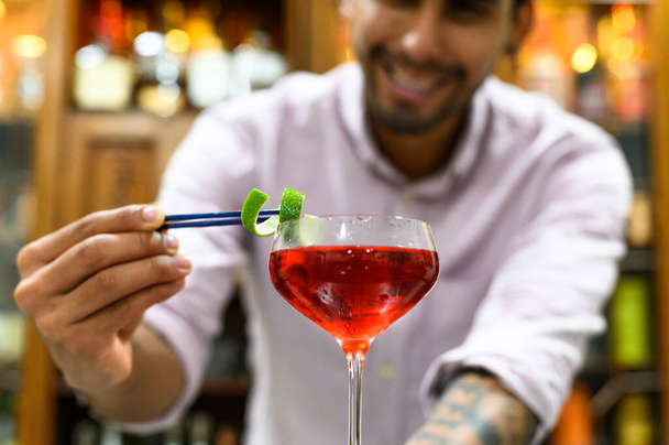 close-up από γυαλί με κόκκινο ποτό που barman ακρίβεια διακοσμούν με φλούδα πορτοκαλιού. - Φωτογραφία, εικόνα