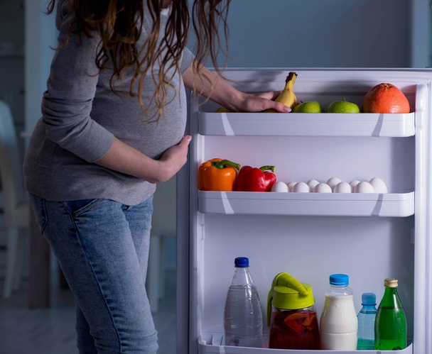 Pregnant woman near fridge looking for food and snacks at night - 写真・画像